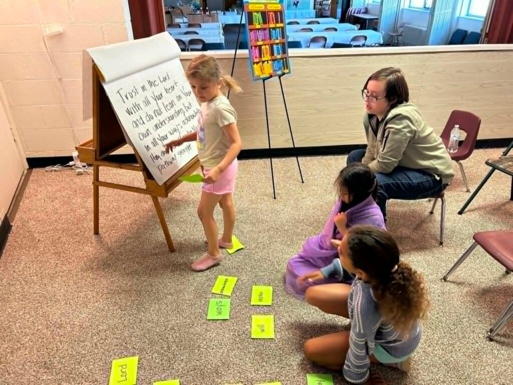 A child points to a Bible memory verse on an easel